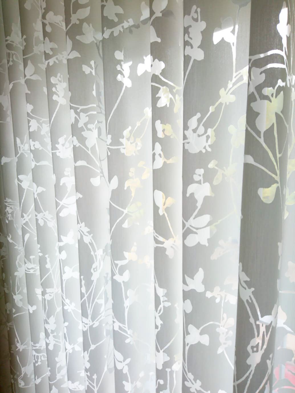Eine Nahaufnahme eines weißen Vorhangs mit einem Blumenmuster.