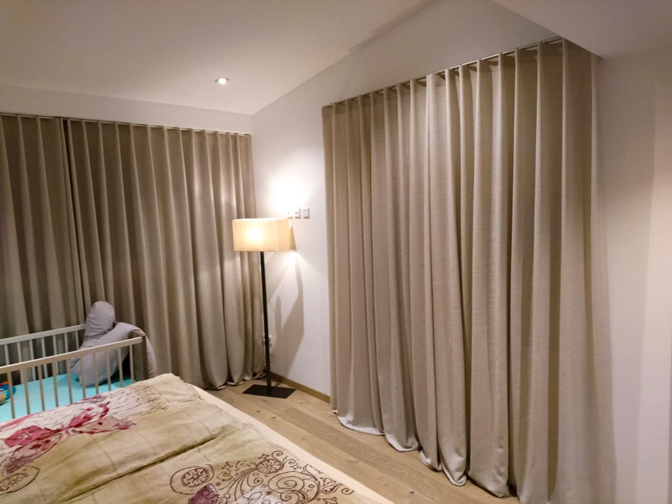 Ein Schlafzimmer mit Bett, Lampe, Kinderbett und Vorhängen.