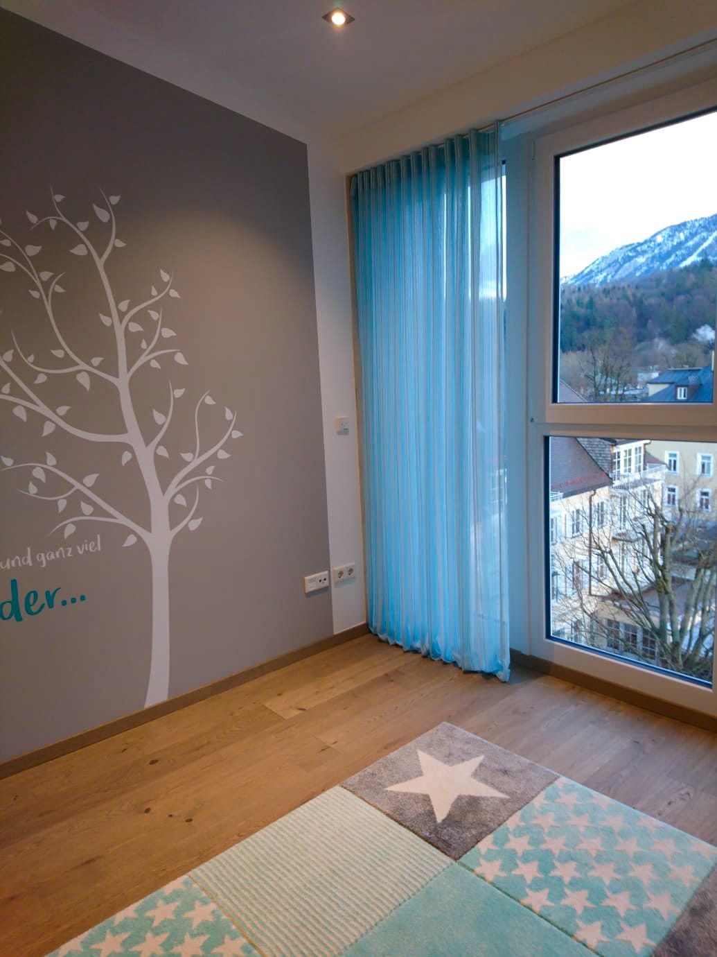 Ein Zimmer mit einem großen Fenster und einem Baum an der Wand