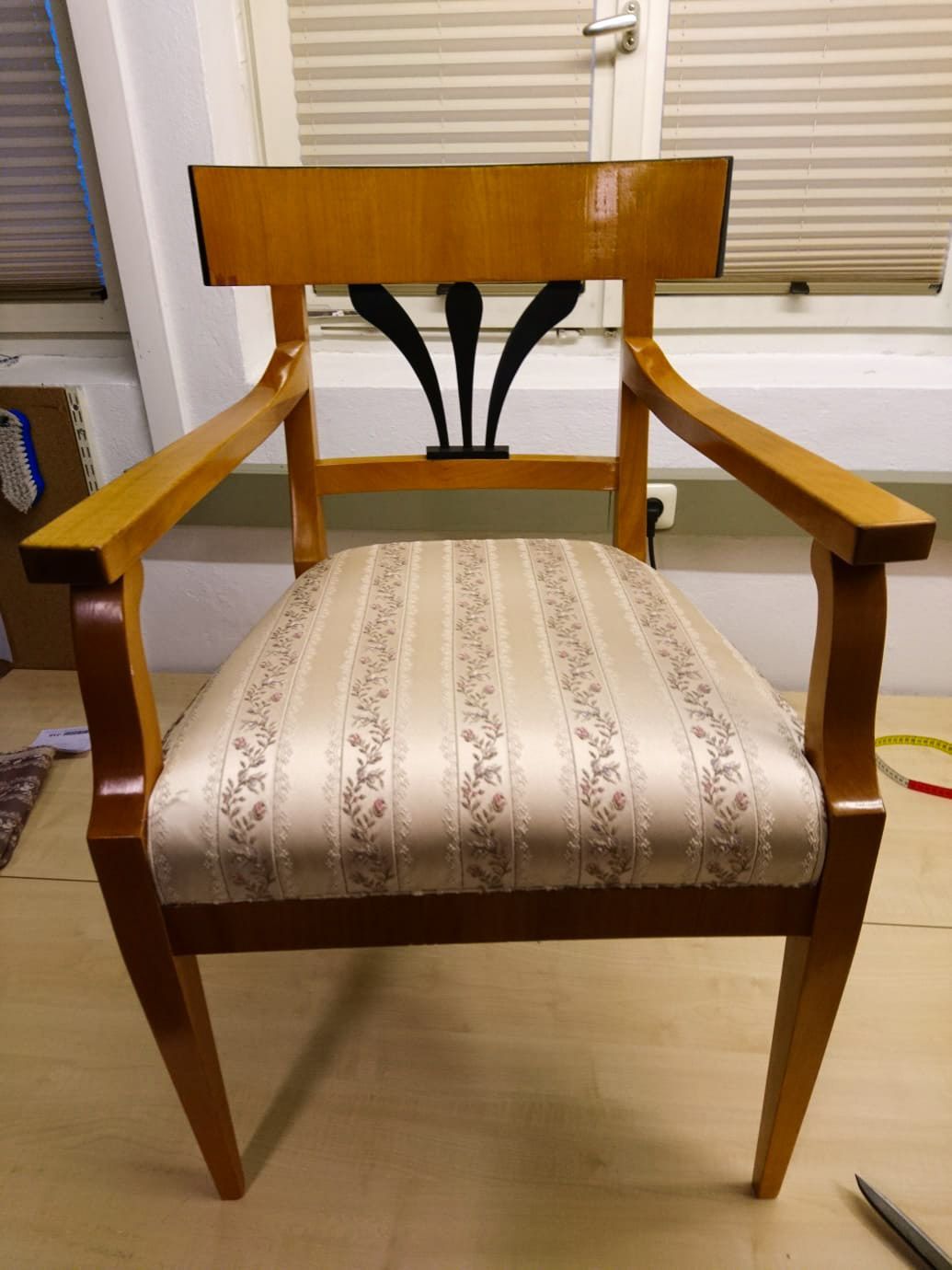 Ein Holzstuhl mit gestreifter Sitzfläche steht vor einem Fenster