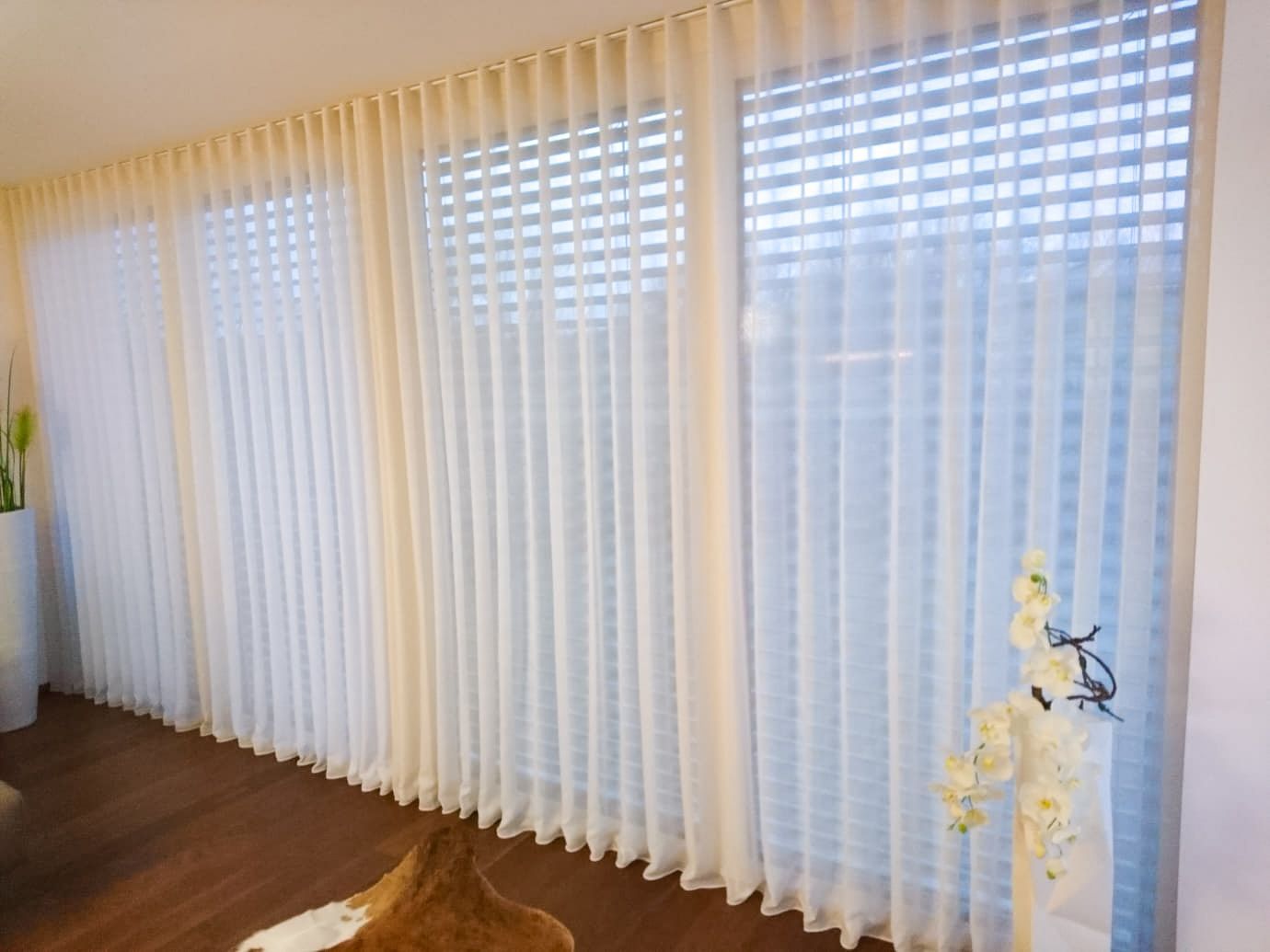 Ein Wohnzimmer mit großem Fenster und weißen Vorhängen.