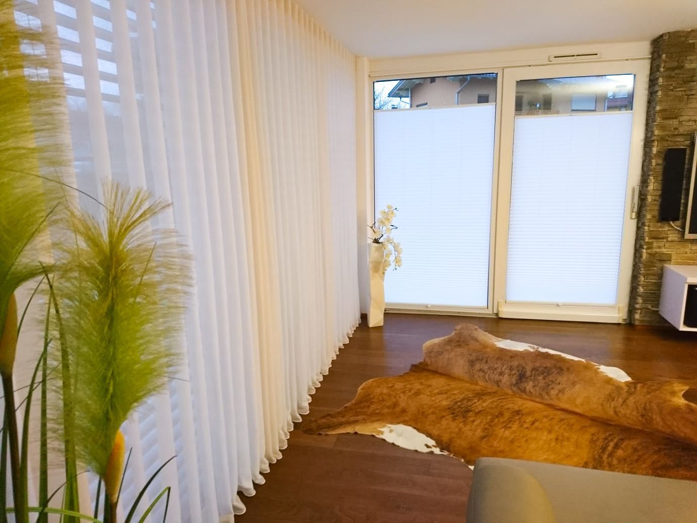 Ein Wohnzimmer mit einem braunen Sofa und weißen Vorhängen