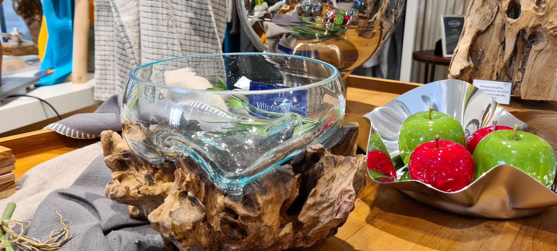 Eine Glasschale, die auf einem Stück Holz neben einer Schale mit Äpfeln steht.