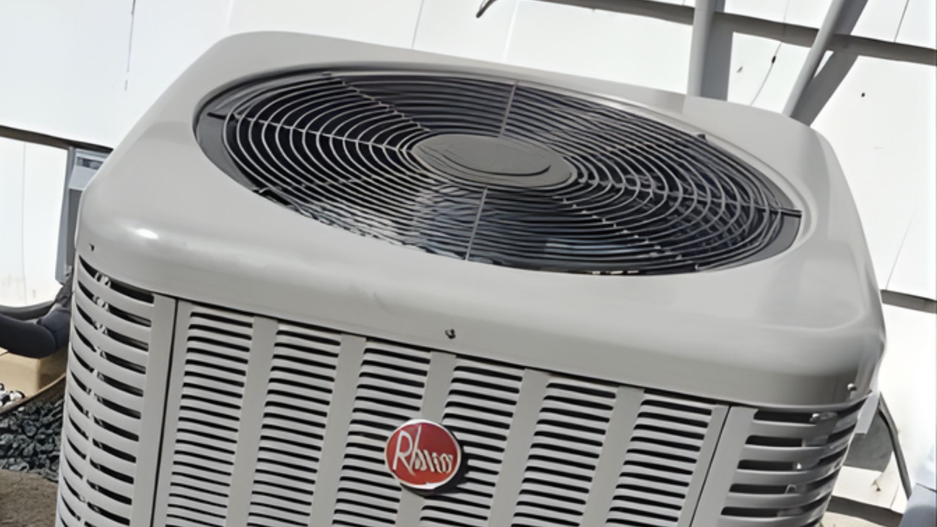 A light-gray Rheem air conditioning unit sits outside near a white-sided house.