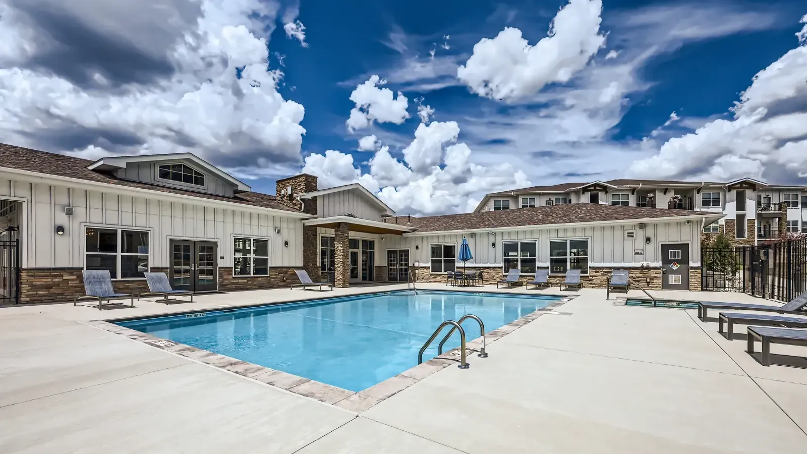 Outdoor apartment community pool with lounge chairs and a clubhouse in the background.