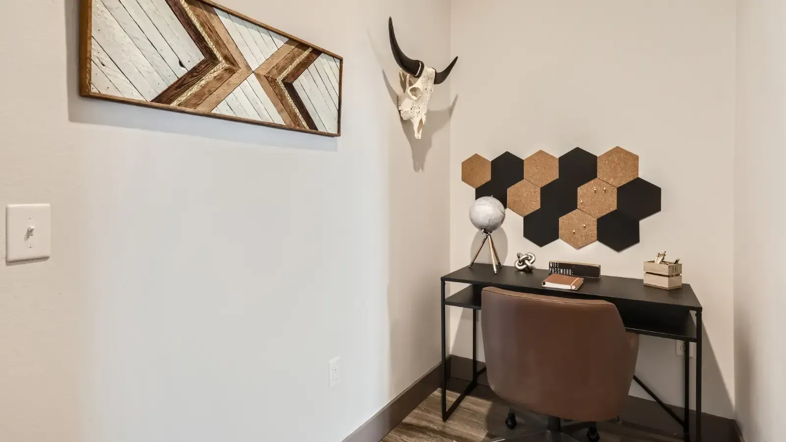 Small home office corner with a black desk, cork hexagon wall decor, and a brown chair.