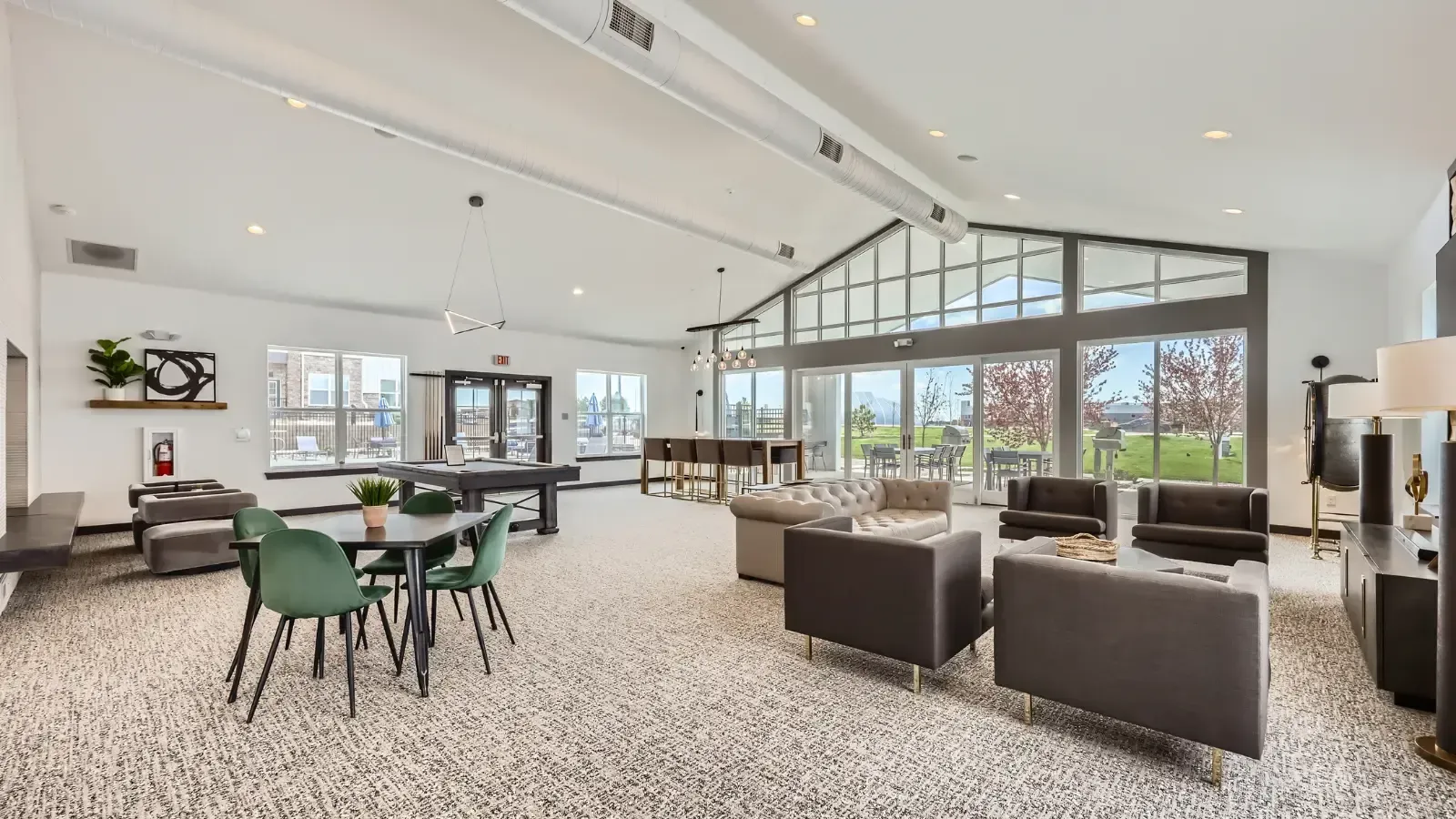 Spacious community lounge with modern seating, tables, and large windows opening to an outdoor patio.