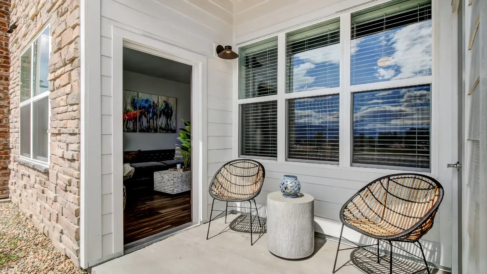 Balcony seating area with two wicker chairs and a round textured table, door to living room open.