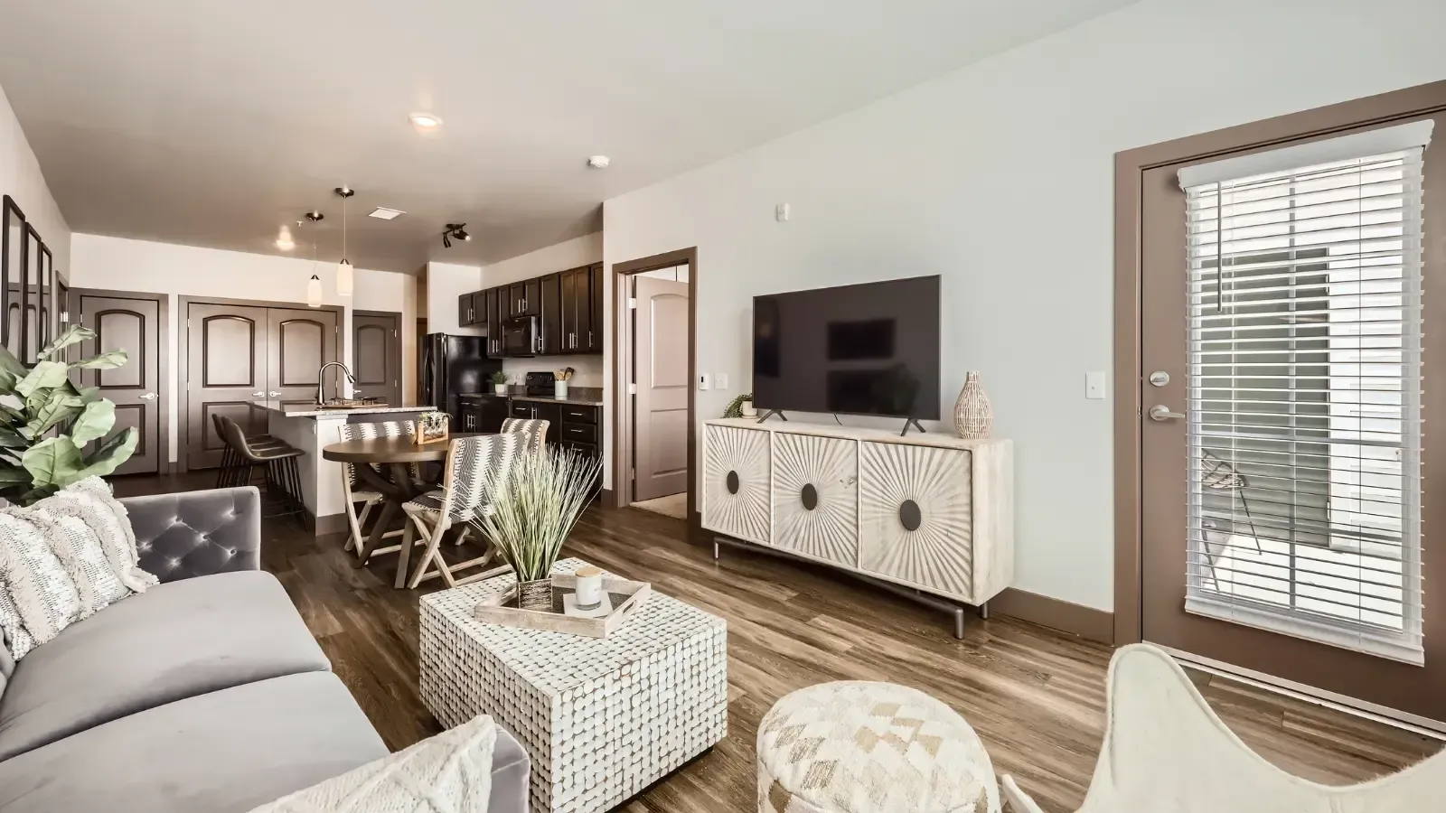 Open-concept living room and kitchen in a modern apartment with a sofa, TV, dining table, and lounge seating.