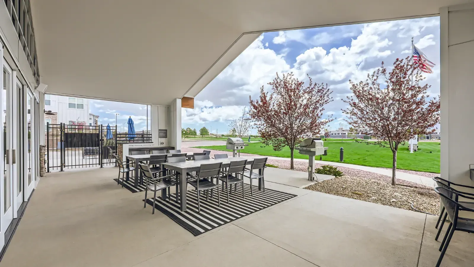 Covered outdoor patio with a long dining table, chairs, grills, and a view of the grassy area.