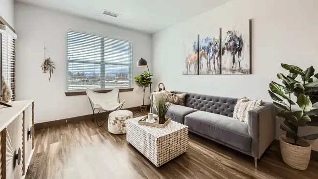 Living room with gray sofa, butterfly chair, and art; neutral tones, natural light.