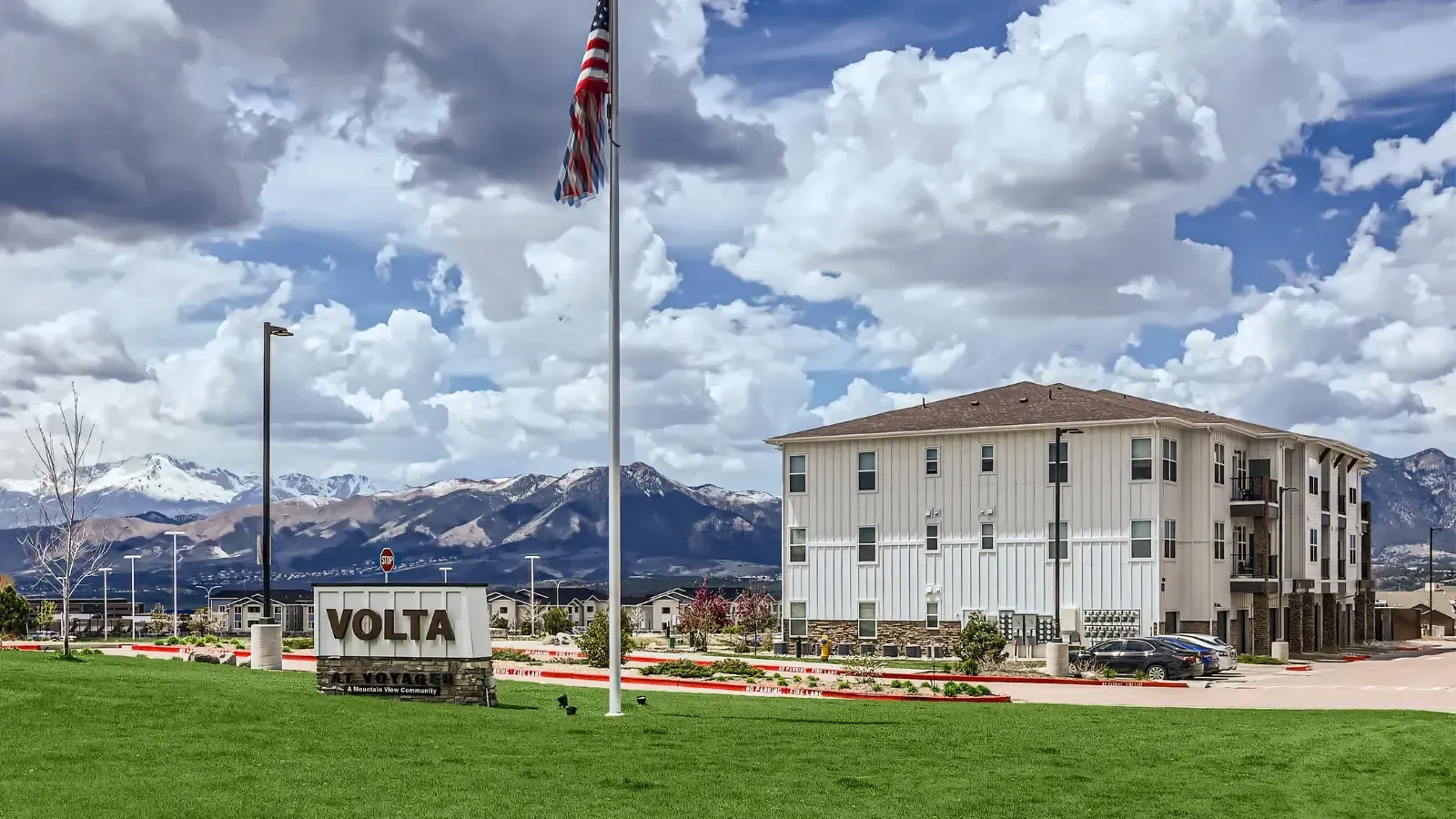 Exterior view of a VOLTA community building with a sign, flagpole, and mountain backdrop.