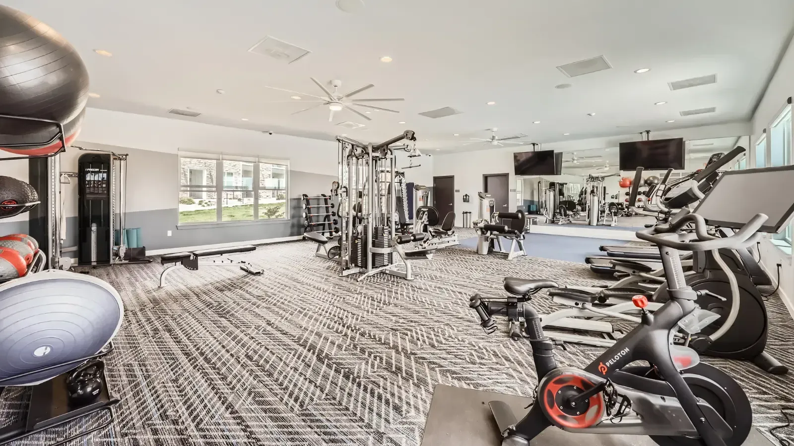 Well-equipped apartment fitness center with cardio machines, free weights, and a large mirror wall.
