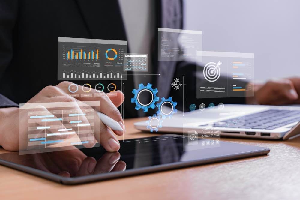 Person using a tablet with overlaid digital data visualizations, sitting at a desk with a laptop.