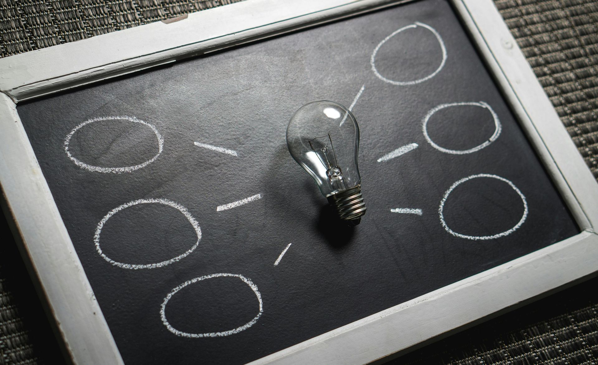 Black chalkboard with white circles and a lightbulb in the center, symbolizing ideas.