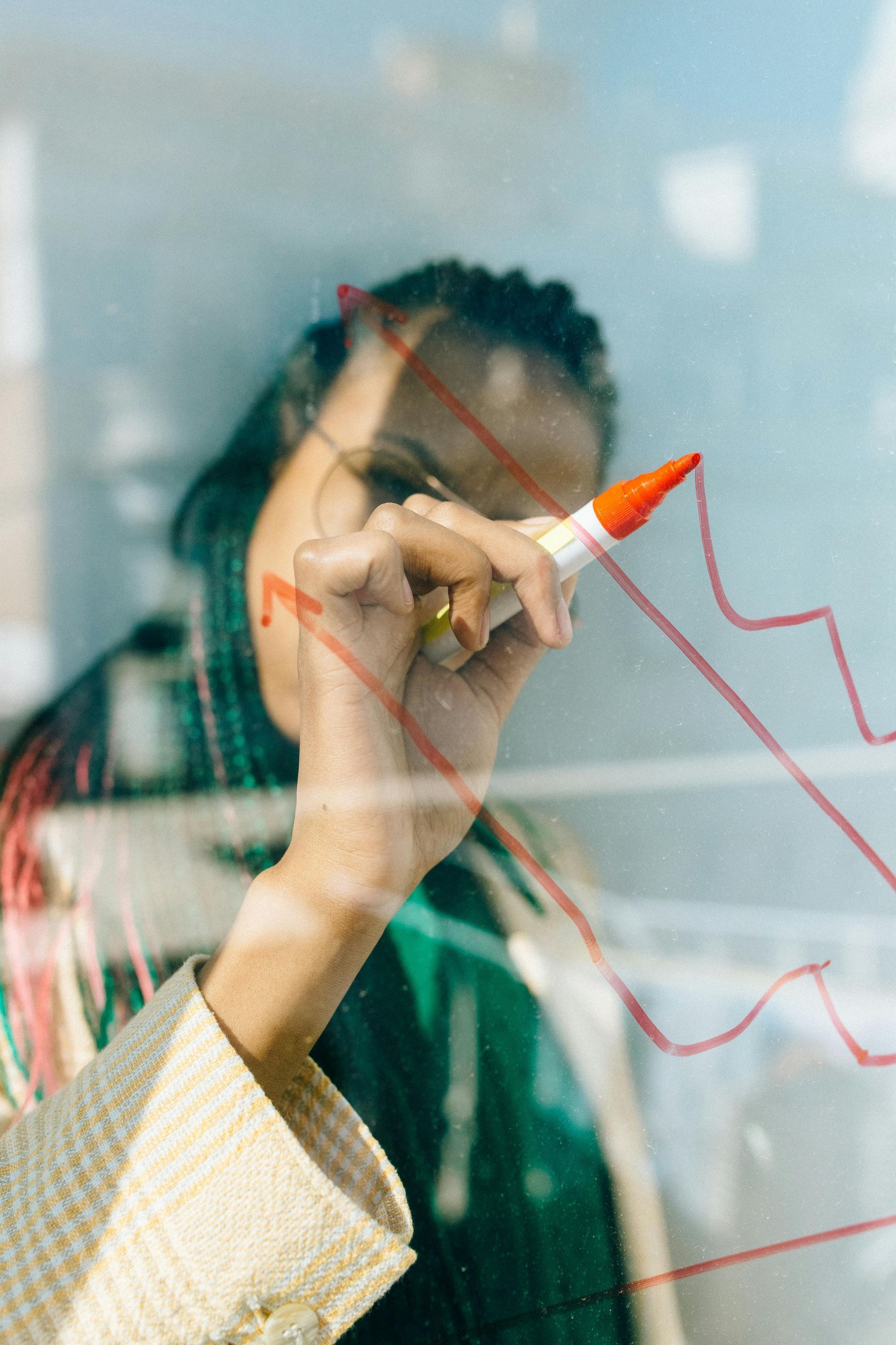 Person drawing a downward trend line with a red marker on a transparent surface.