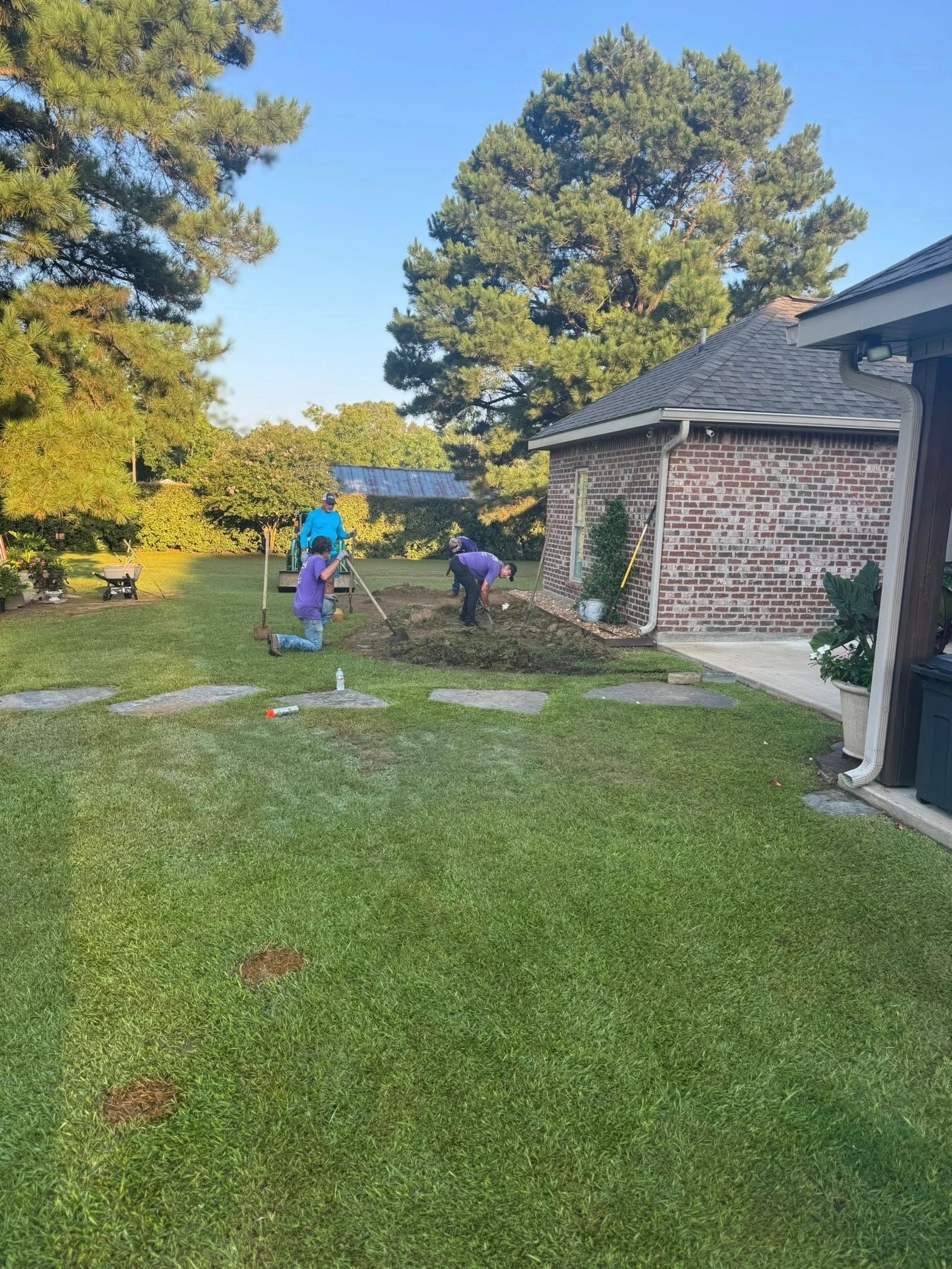 People gardening in a grassy yard near a brick building.