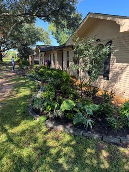 A house with a brick facade and a lush garden in front. A person is working in the garden.