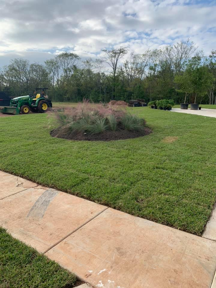 A landscaped lawn with a central flower bed and a tractor; cloudy sky in the background.