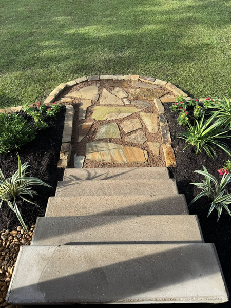 Stone path and concrete steps leading to a grass yard, with flower beds on each side.