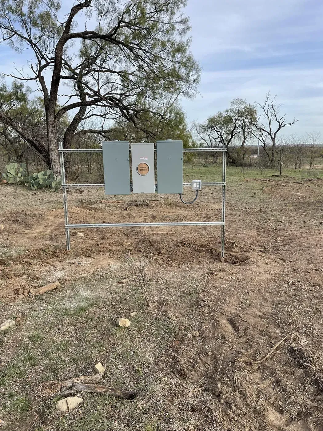 Steel targets on a stand in a field with trees in the background under a cloudy sky.