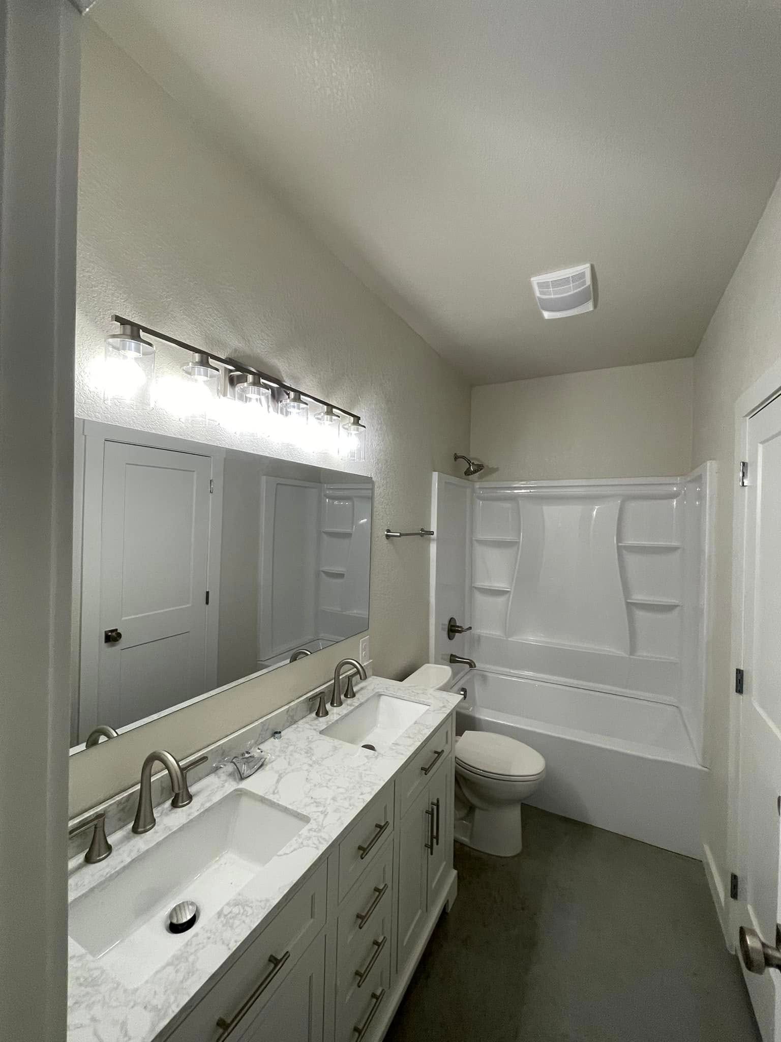 A modern bathroom with a double vanity, large mirror, and a shower/tub combo.