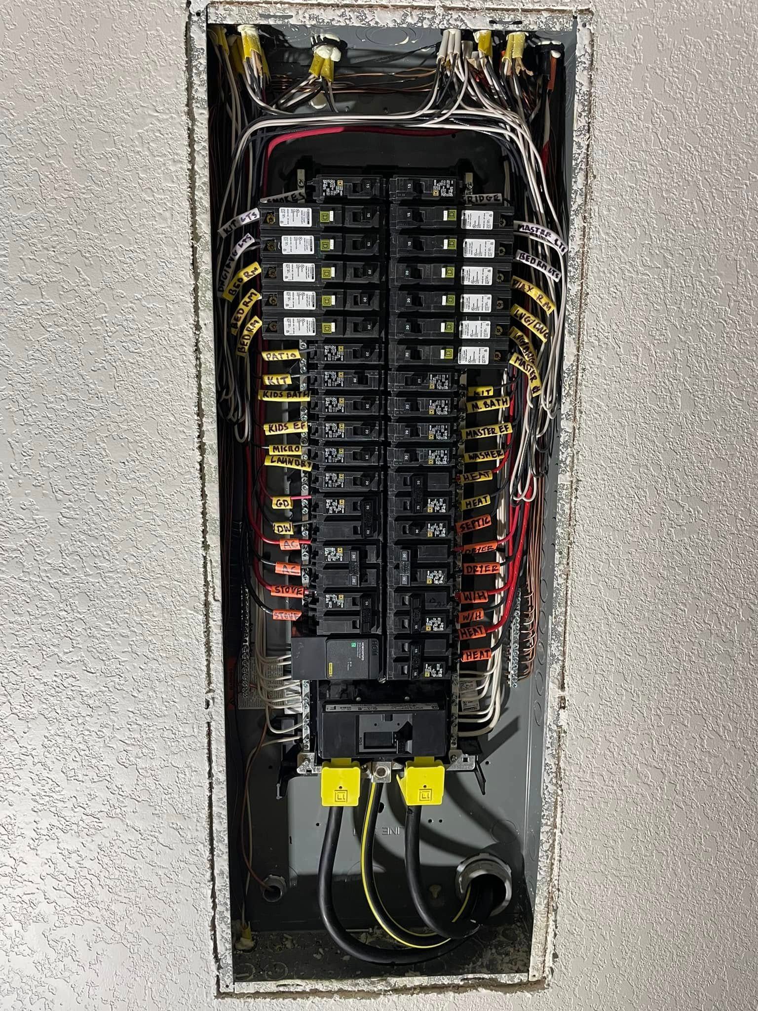 Electrical panel with multiple circuit breakers and wiring inside a recessed metal box.