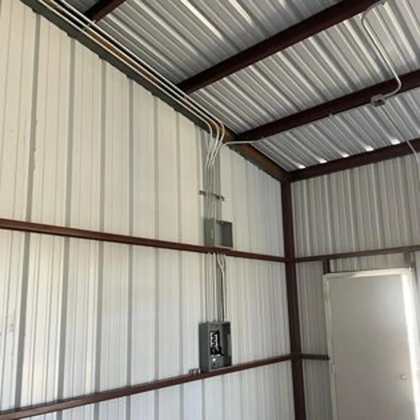 Electrical conduit and paneling inside a metal-framed structure, with a white door visible.