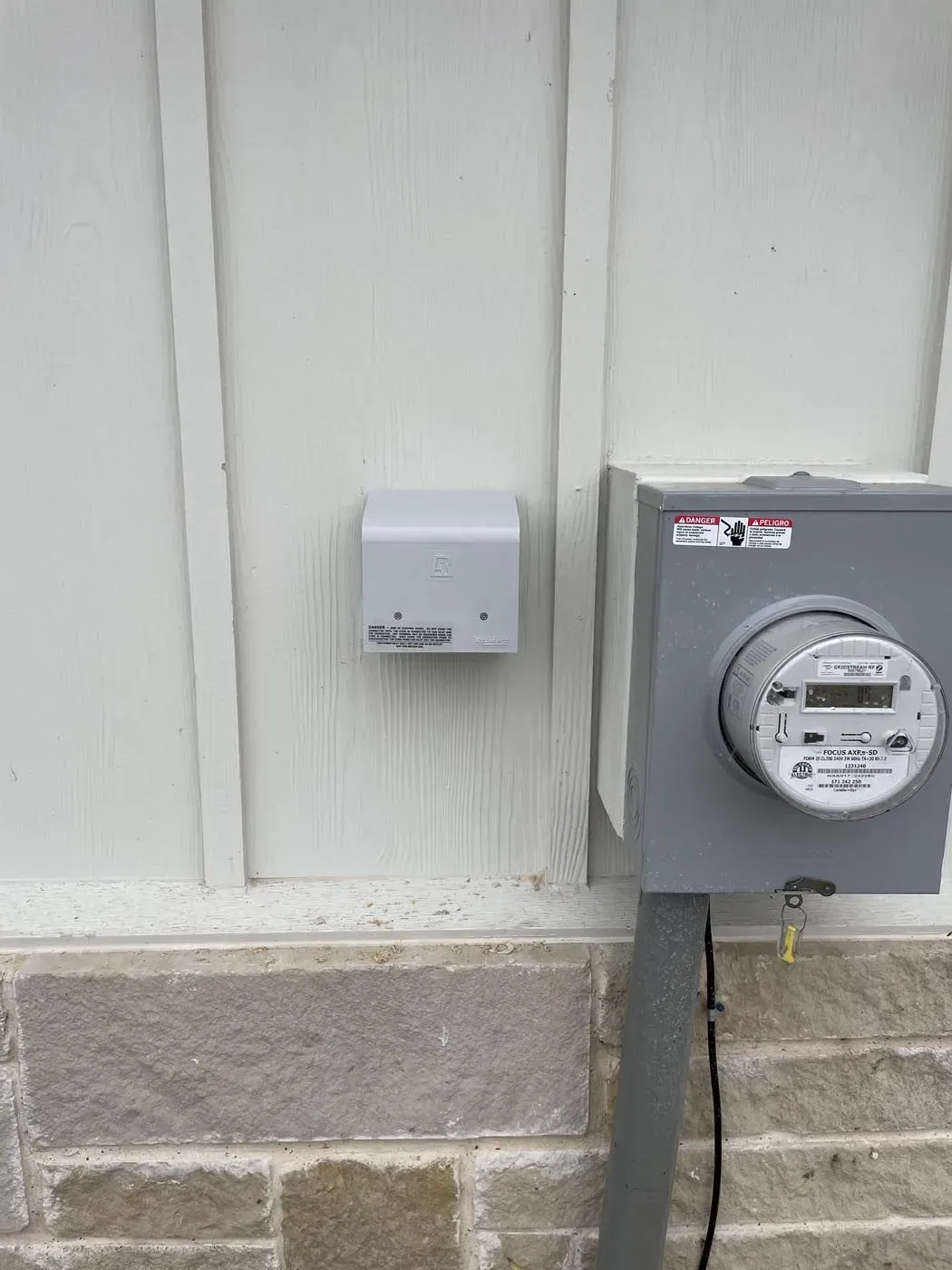 Outdoor electrical meter and outlet box on a white wall with stone base.