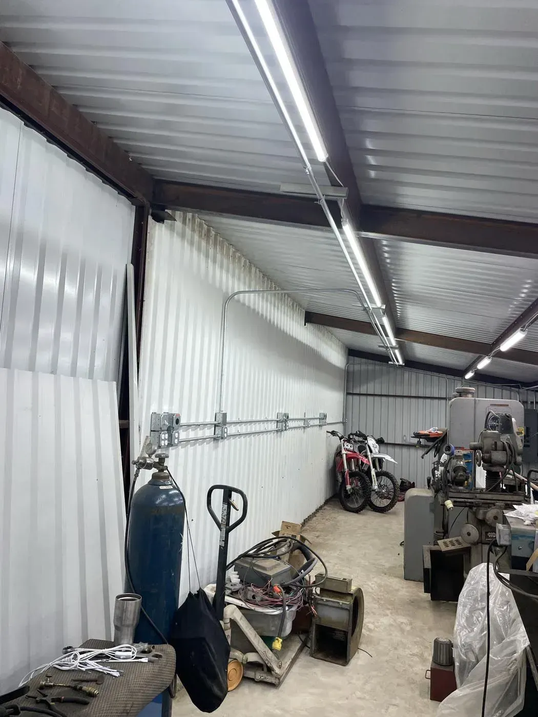 Workshop interior with metal walls, overhead lighting, tools, and a motorcycle.