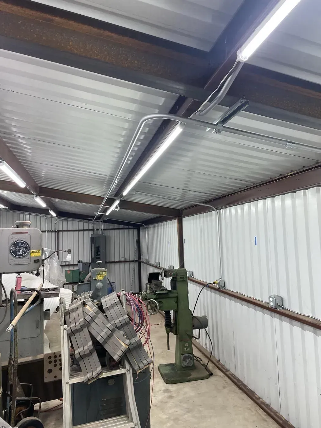 Workshop interior with metal ceiling, walls, and fluorescent lights. Tools and machinery visible throughout the space.