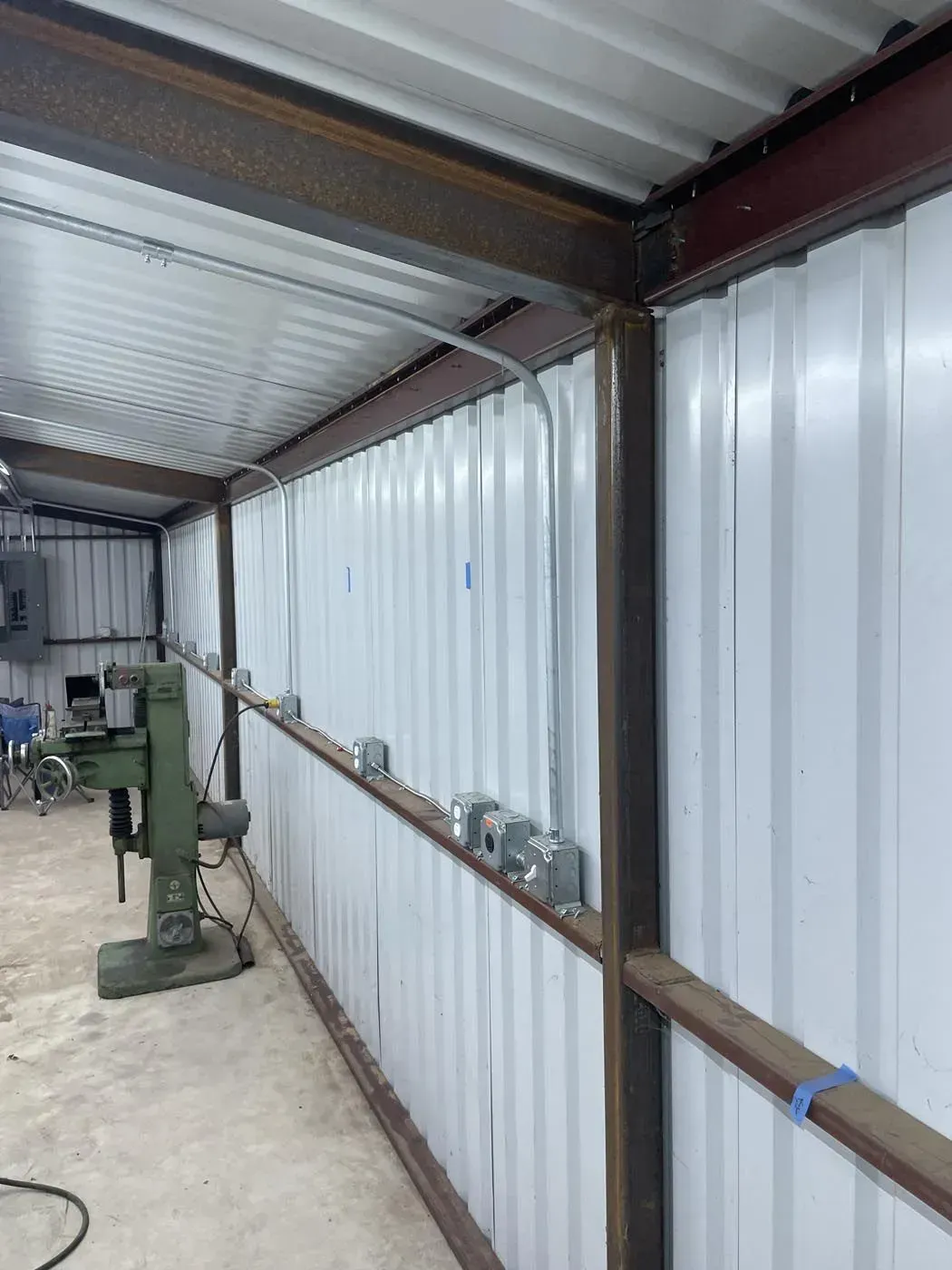 Metal-framed structure with corrugated white walls and roof. Electrical boxes line the interior.