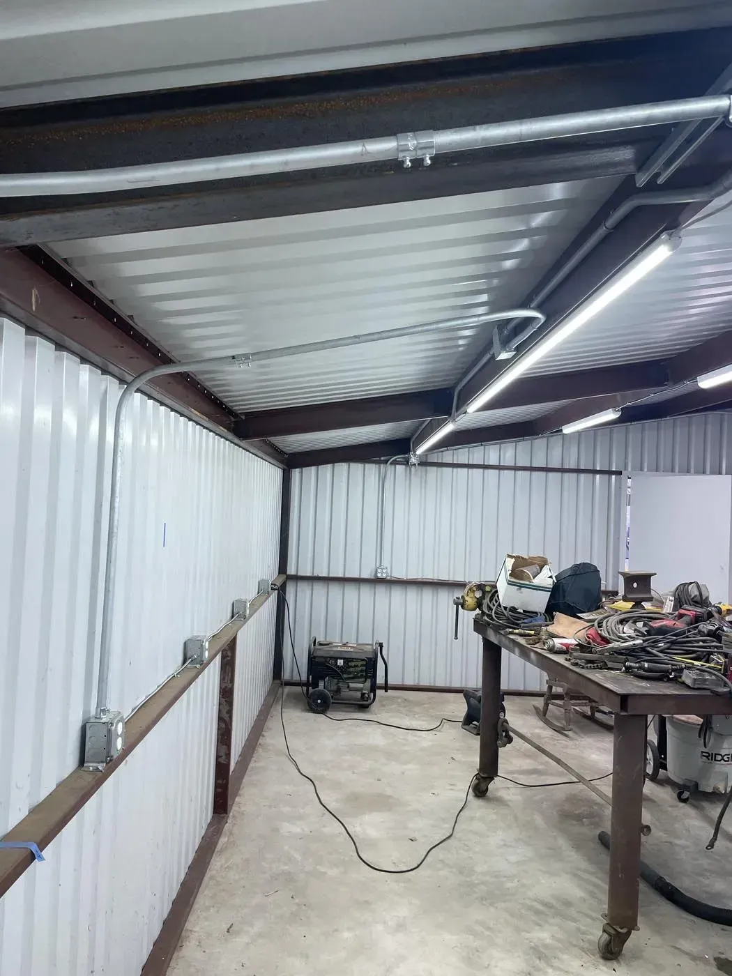 Workshop interior with corrugated metal walls, overhead lighting, and electrical conduit. 