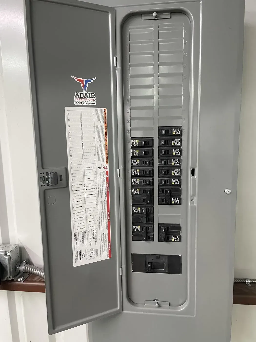 Gray electrical panel with opened door, showing circuit breakers.