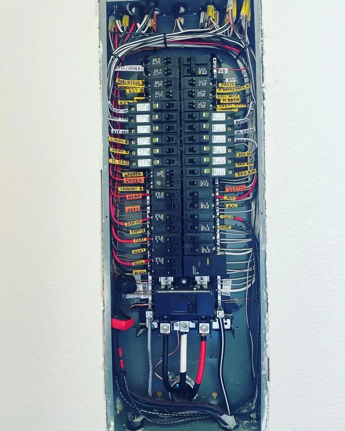 Electrical panel with numerous circuit breakers and wires, set in a wall.