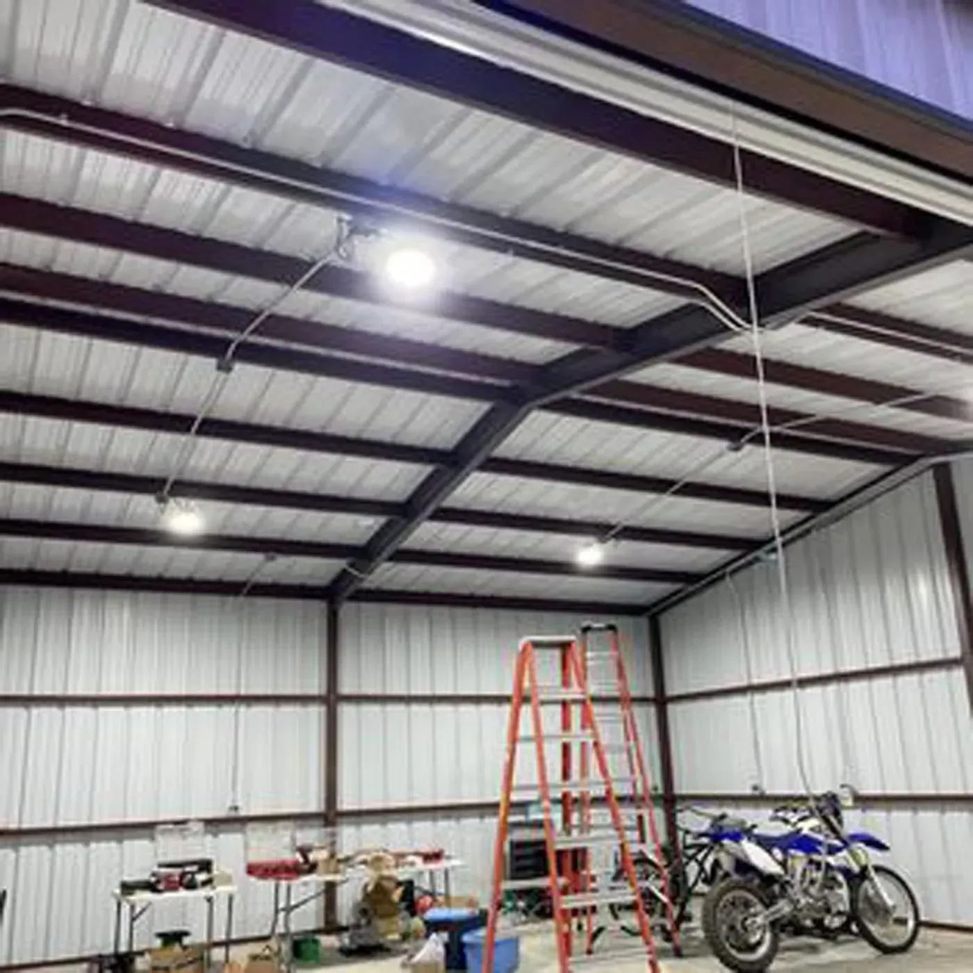 Interior of metal building with lights, ladder, and motorcycles.
