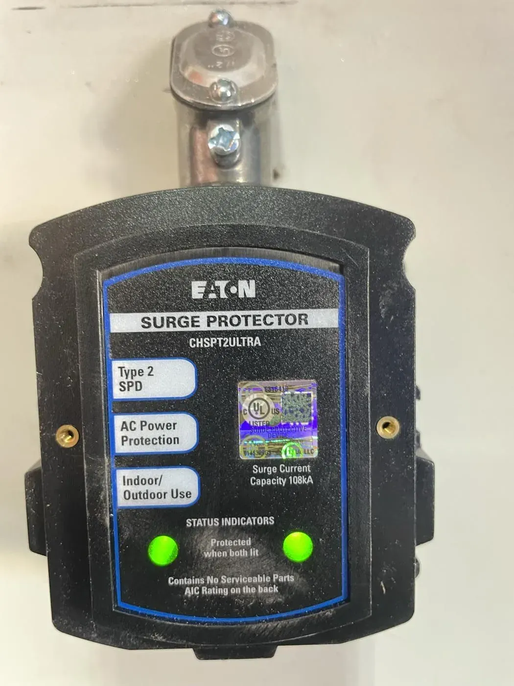 Eaton surge protector box on a wall. Black with a blue label, two green lights, and a silver conduit.