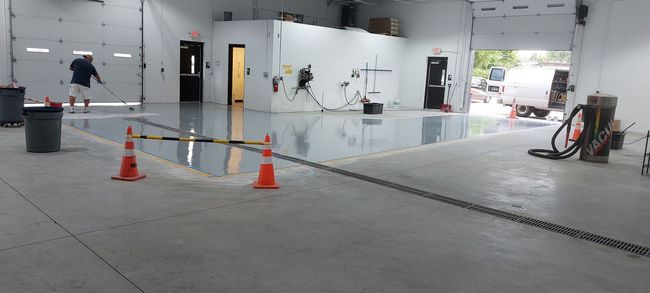 A person applying a glossy epoxy finish to a garage floor, marked by traffic cones and work equipment.