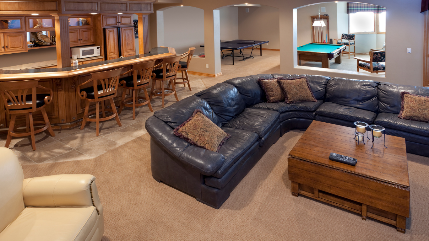 A spacious, finished basement features a bar area, large blue leather sectional sofa, coffee table, and a pool table.