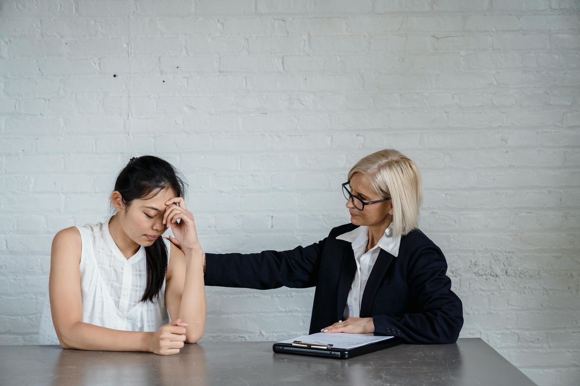 A woman is comforting another woman who is sitting at a table.