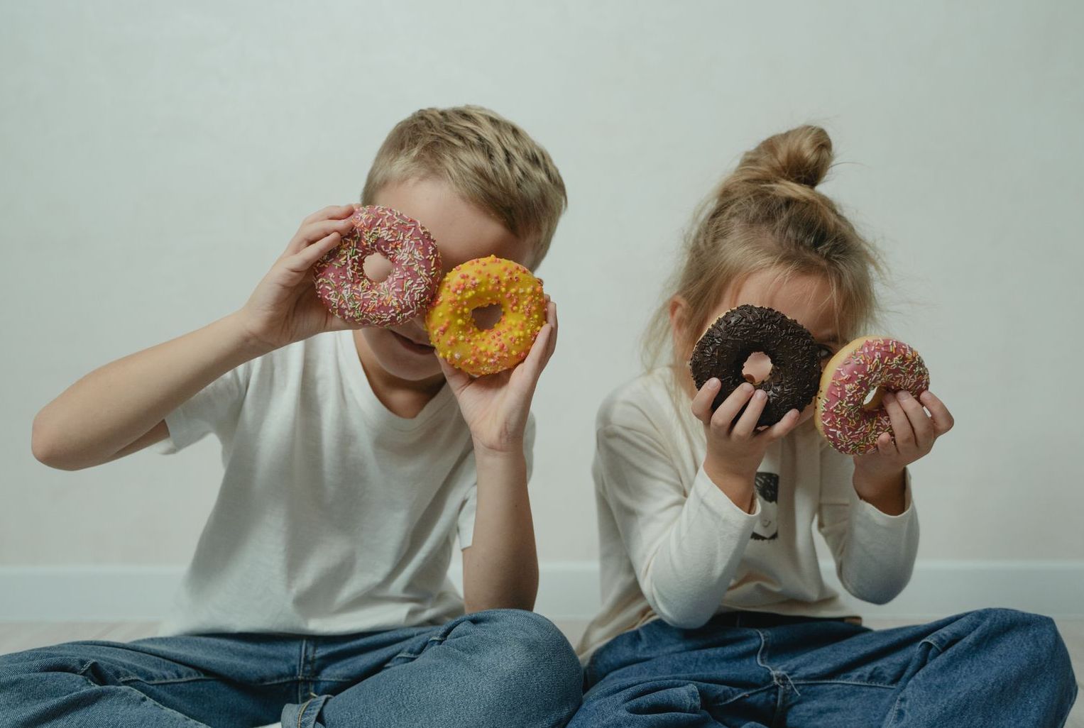 Two smiling children being foolish as they hold doughnuts over their eyes