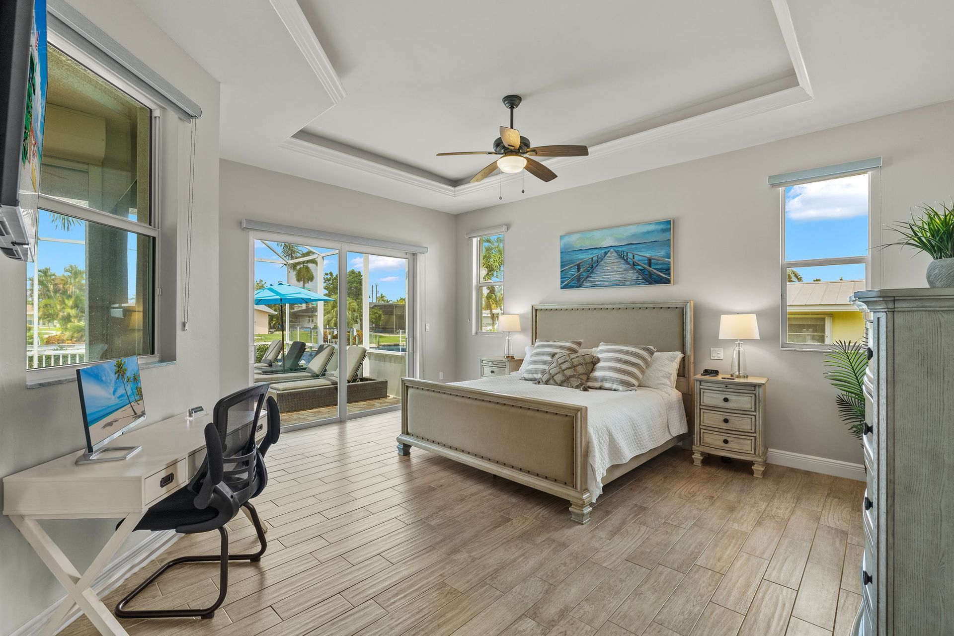 A bedroom with a large bed, desk, chair, and ceiling fan.