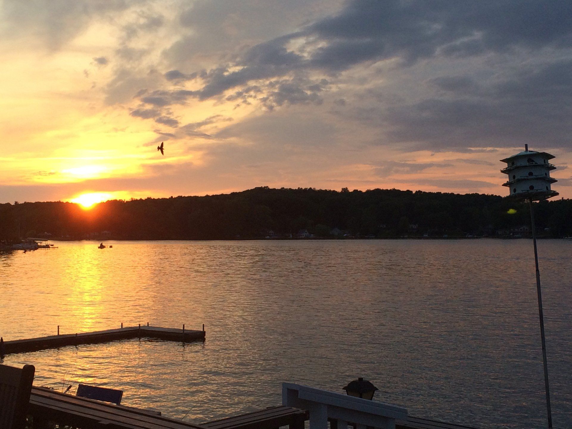 A sunset over a lake with a birdhouse in the foreground