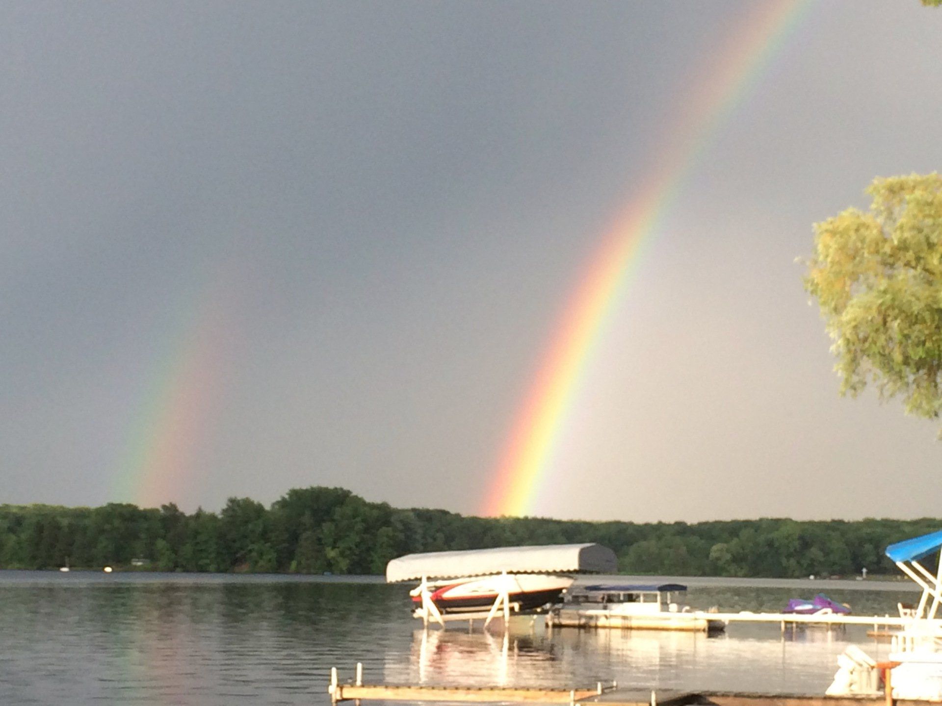A rainbow over a lake with boats docked at the dock