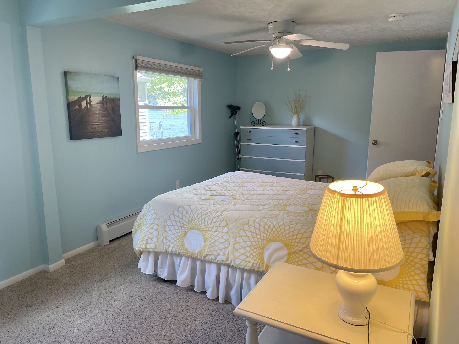 A bedroom with a bed, dresser, lamp, and ceiling fan.