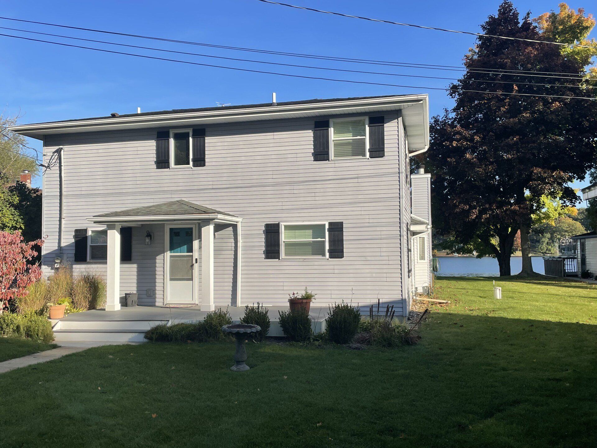 A gray house with black shutters is next to a body of water
