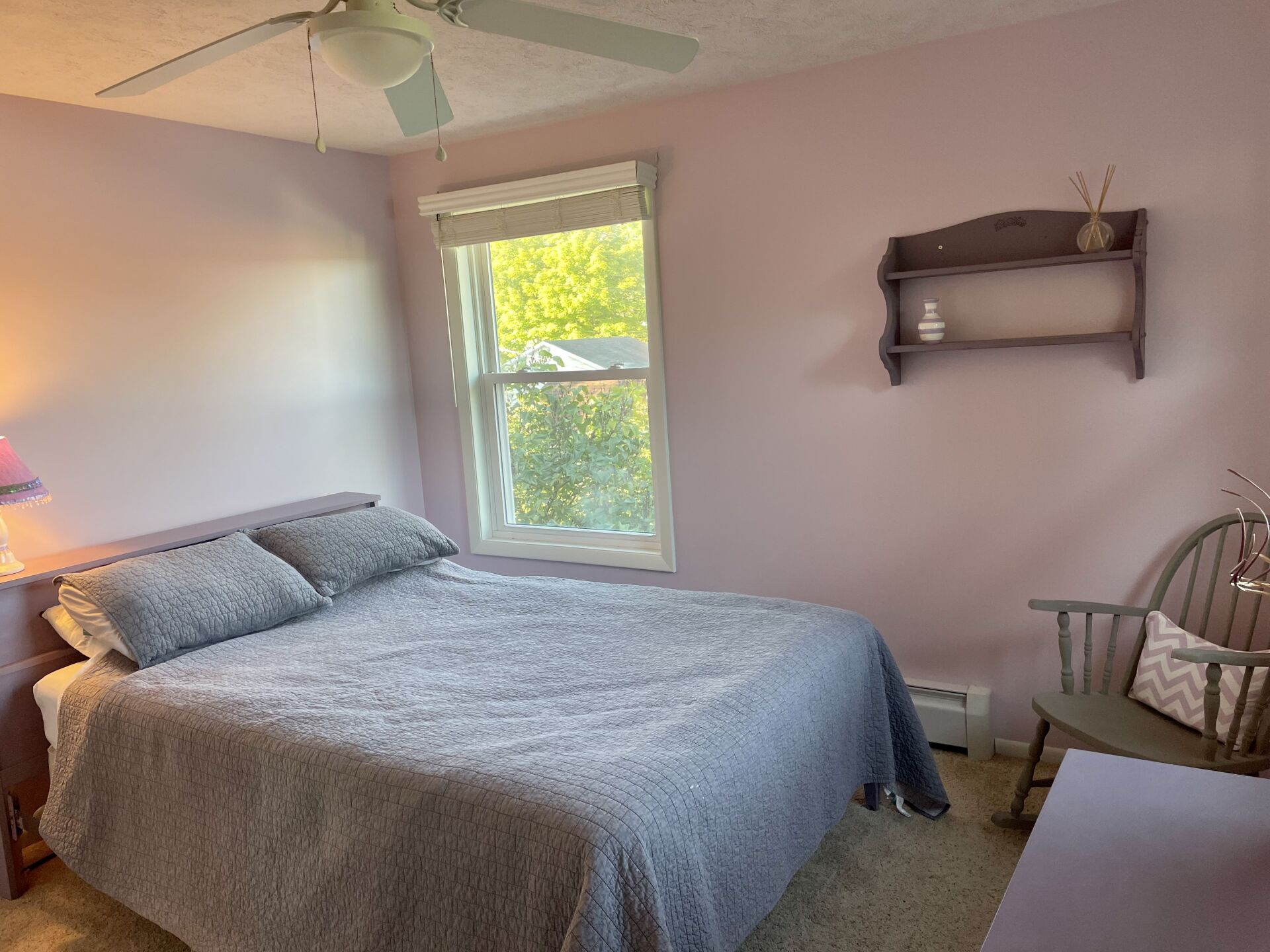 A bedroom with a bed a chair and a ceiling fan