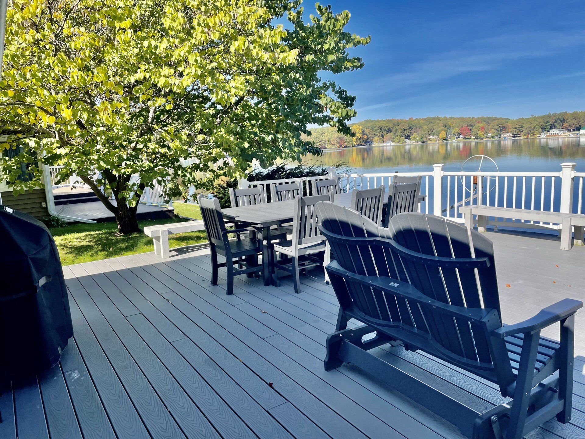 A deck with a swing, table, and chairs overlooking a lake.