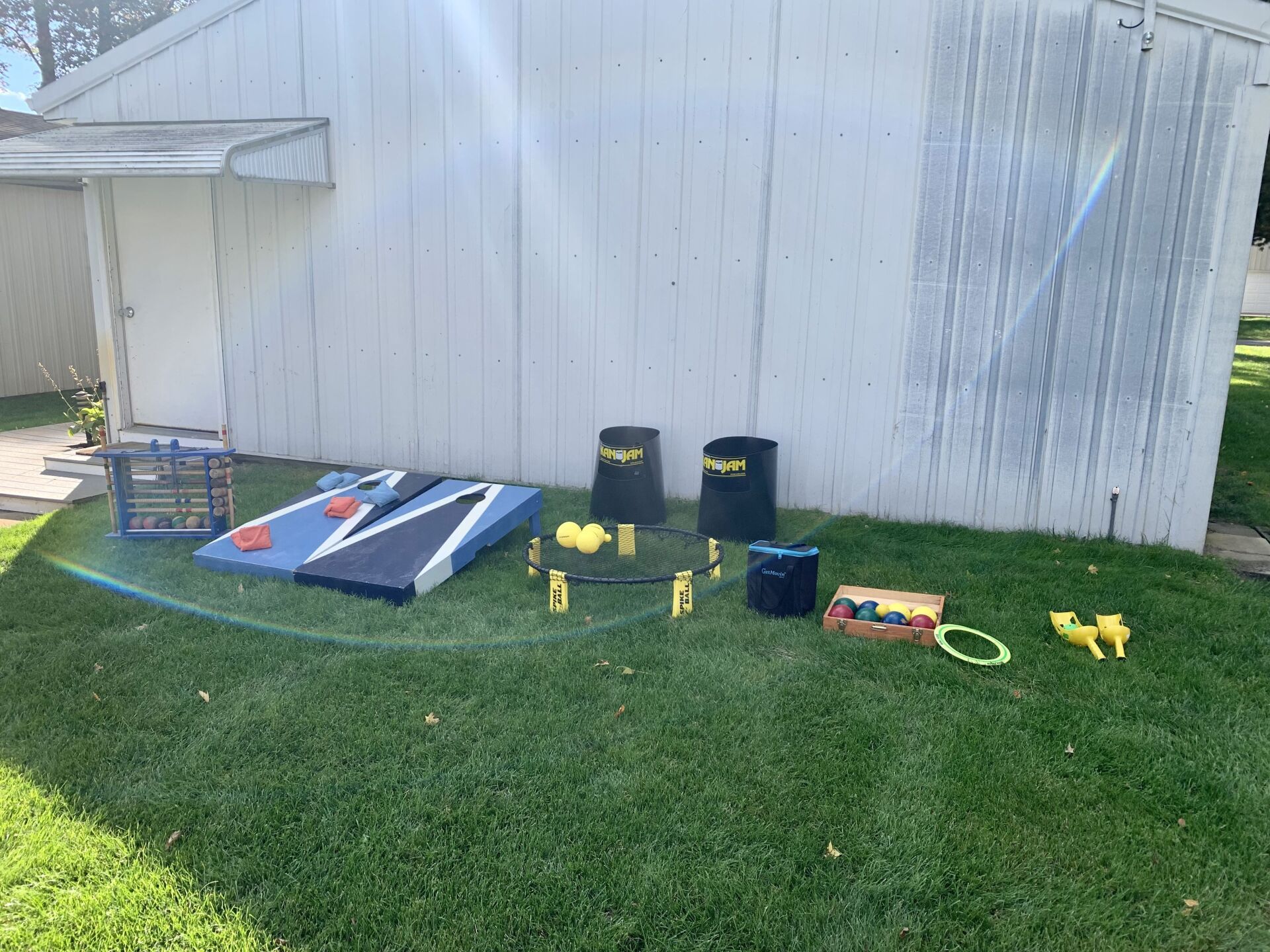 A bunch of games are sitting on the grass in front of a white shed.