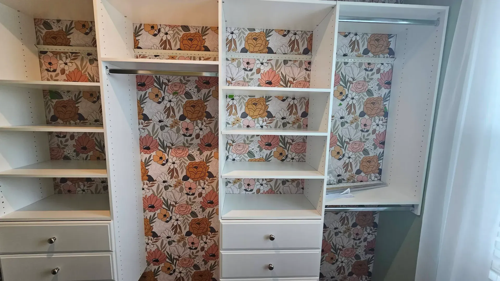 A walk in closet with a floral wallpaper on the wall.